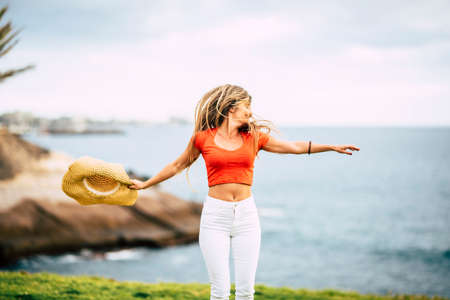Happiness and joyful freedom people concept - young beautiful slim woman with long hair jump and dance in outdoor leisure activity alone with ocean and nature green meadow backgroundの写真素材