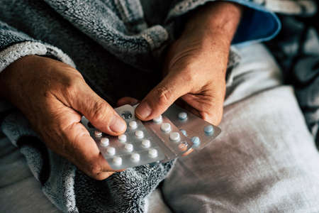 close up of hands of senior man taking or choosing a pillow to cure his fever and to be healthy and not sick - pensioner and retired alone at home - pharmacy usually life for old peopleの写真素材