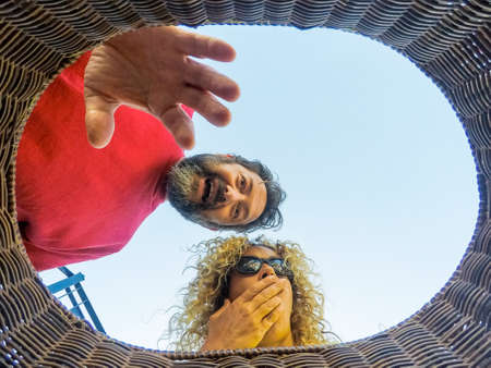 Adult caucasian couple look inside a bucket and do surprised expression - indoor inside wide view - surprise concept with blue sky in background and man and womanの写真素材