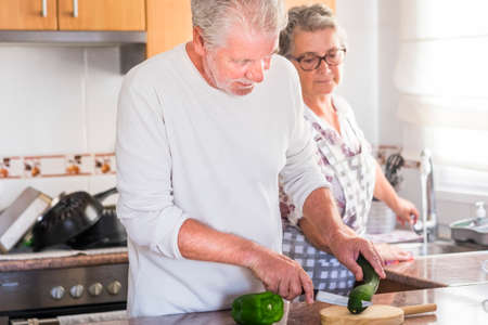 Beautiful senior adult caucasian people couple at home working together in the kitchen - equal rights concept with man and woman cooking - happy real life after retiremen - mature lifestyleの写真素材