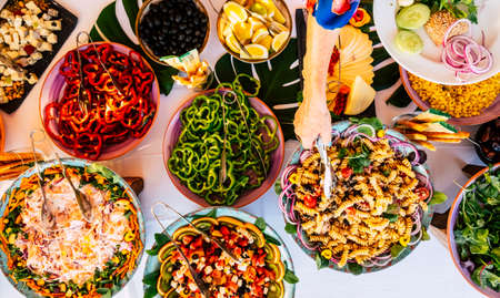 Vertical view of senior woman hand serving food on a dish from catering table during party celebration - catering and restaurant concept with mixed chef food on a table -coloured background and togetherの写真素材