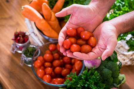 Close up of hands holding fresh and red colored cherry tomatoes and various mix vegetables in backgraound cof healthy food nutrition concept lifestyleの写真素材