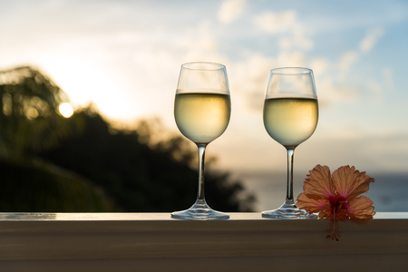 Romantic moments in summer at sunset with two glasses of white wine - Relaxing romantic holiday concept with beautiful view of tropical beach and coastの写真素材