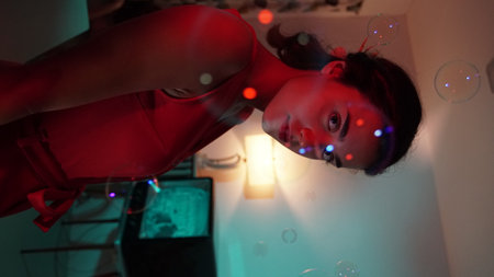 Young woman in red dress playing with soap bubbles in the dark roomの写真素材