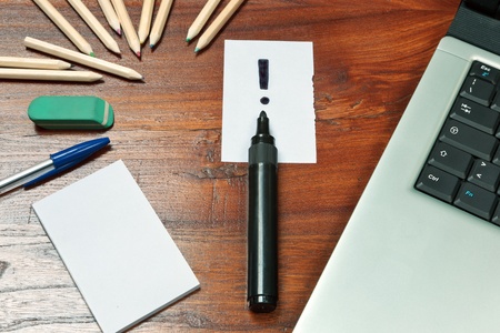 Exclamation mark over a black pen on a wooden desk with computer, pen and other  paper noteの写真素材