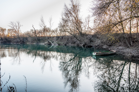 An Autumnal day on the river, with a boat, trees and reflectionsの写真素材