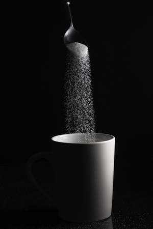 White granulated sugar pouring from a spoon into a white cupの写真素材