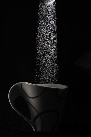 White granulated sugar pouring from a spoon into a white cupの写真素材