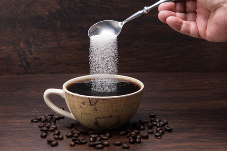 Sugar pours into Coffe Cup with Coffe  Beans on wooden backgroundの写真素材