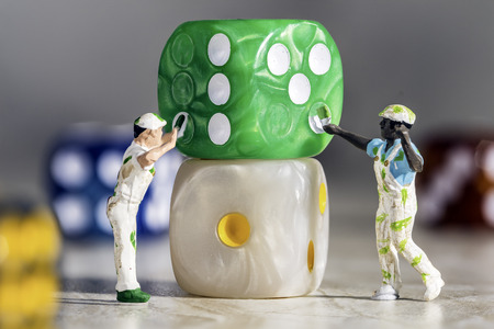 Two Miniature People Painters Painting green Dice with White Pips On a Grey Marble Background. Shows teamworkの写真素材