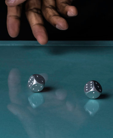 A hand Throwing two silver steel dice in a casino. They are rolling on a blue background which shows reflectionsの写真素材