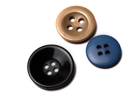 Close up of three buttons. Black, gold, blue in color on white background