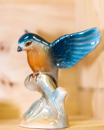 Colorful ceramic porcelain glazed bird landing on tree branch. Small Figurine on brown background. Spread your wings.の写真素材