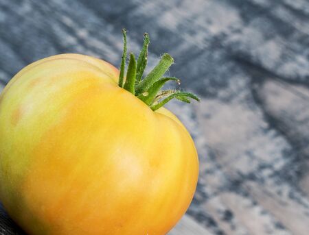 Big fresh yellow tomato isolated on wood  background. Showing green stemの写真素材