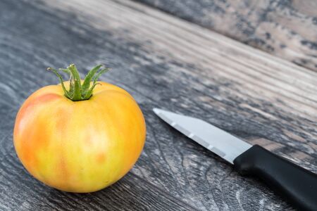 Big fresh yellow tomato with knife isolated on wood  background.の写真素材
