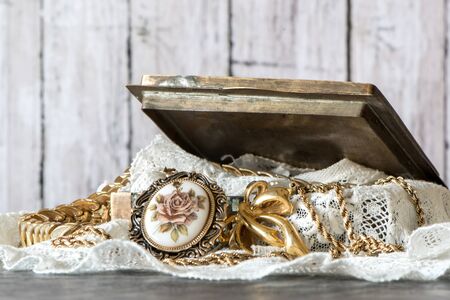 Metal Open Jewelry Box with pile of  golden jewelry and lace against wood backgroundの写真素材