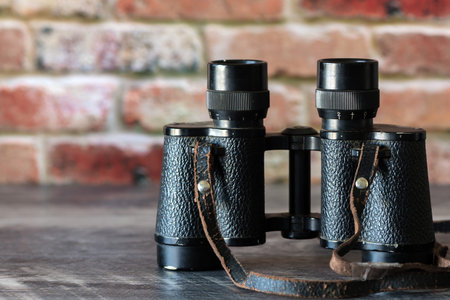 old binoculars with strap against brick wall . Retro travel Concept with grungy look.