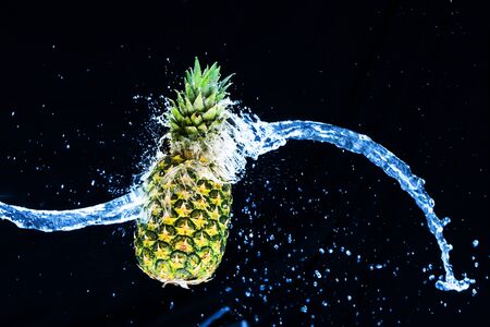 Fresh pineapple gets splashed with water on black background. Concept of summer, health and funの写真素材