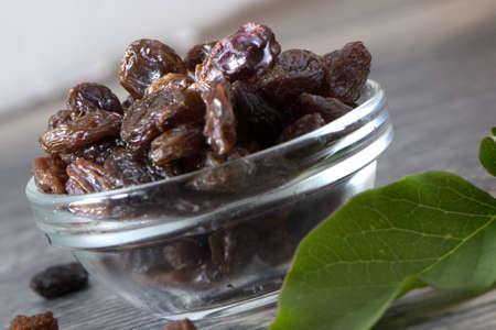 Raisins in glass bowl with green leaf on wood. Healthy foodの写真素材