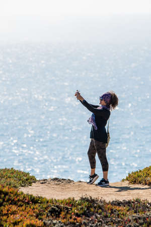 Woman taking selfie on rock with ocean in background. Bodega Bay Northern Californiaの写真素材