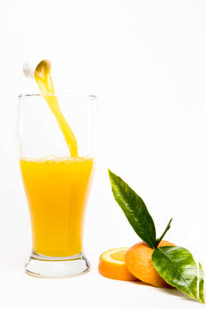 Pouring orange juice into glass with pieces of oranges and greenorange  leafs on black background. Abstract.の写真素材