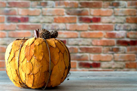 Decorative pumpkin made of yellow leafs isolated against red brick wall background. Thanksgiving conceptの写真素材