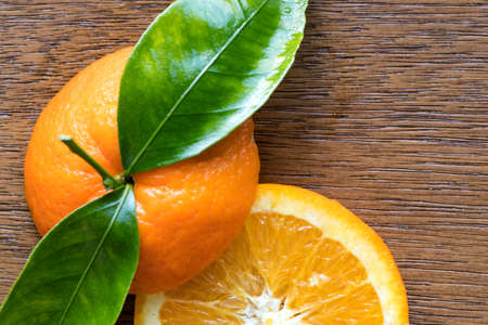 Fresh orange fruit with cut in half slice and green leaf isolated on wood background . Top view. Flat lay. Close upの写真素材