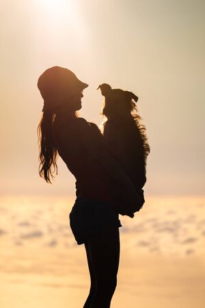 Silhouette of girl with puppy on sunsetの写真素材