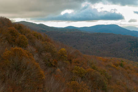 Mountain landscape with forests of green, red, orange and yellow colors that contrast the landscape. Beautiful views of nature with blue and gray skies.の写真素材