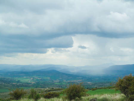 Landscape of green plains with a cloudy sky over distant mountainsの写真素材