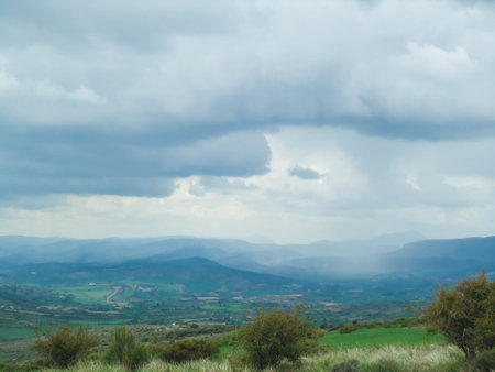 Plain of agricultural fields with a cloudy blue sky over distant mountainsの写真素材