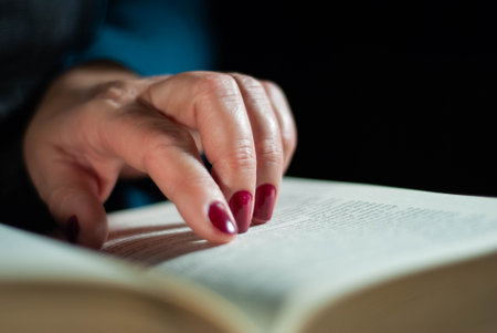 Hands holding a book that an elderly woman is reading using her fingers on the lines filled with wordsの写真素材