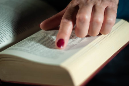 Hands holding a book that an elderly woman is reading using her fingers on the lines filled with wordsの写真素材