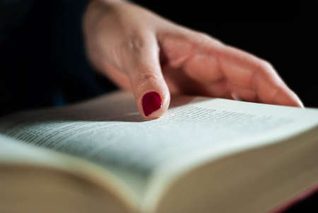 Hands holding a book that an elderly woman is reading using her fingers on the lines filled with wordsの写真素材