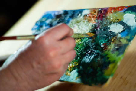 Painter's hands taking a paint brush from his palette to paint an oil paintingの写真素材