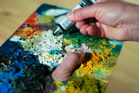 Painter's hands taking a paint brush from his palette to paint an oil paintingの写真素材