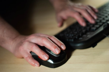 Hands typing on a computer keyboard with a mouse, close-up in front of the screen
