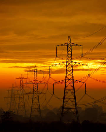 A row of power pylons against a misty orange skyのeditorial素材