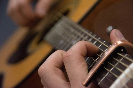 Guitar deck and guitarist hands closeup. Capo on the fretboard of a guitar. Blurred guitar background.の写真素材