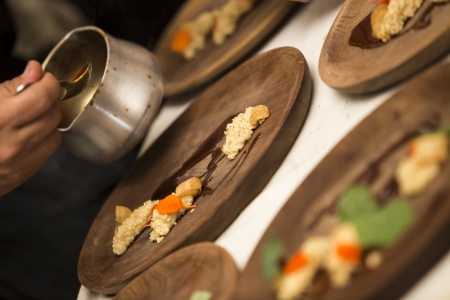 Meal in a wooden plate an people working on the preparation の写真素材