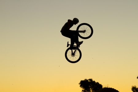Silhouette of a young man performing a radical mountain bike jumpの写真素材