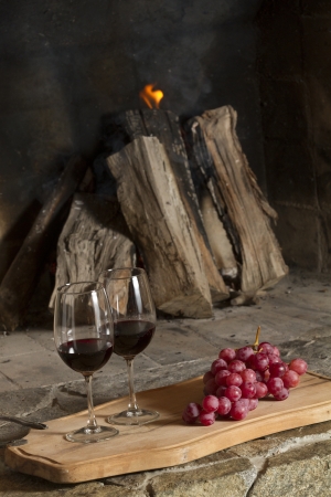 Wine glasses, Grapes, cork and a bottle of wine over a wooden table with fire on the background の写真素材