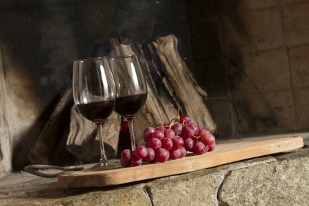 Wine glasses, Grapes, cork and a bottle of wine over a wooden table with fire on the background の写真素材
