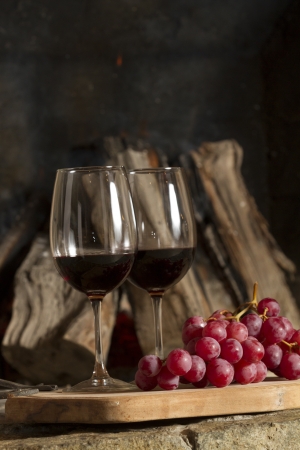 Wine glasses, Grapes, cork and a bottle of wine over a wooden table with fire on the background の写真素材