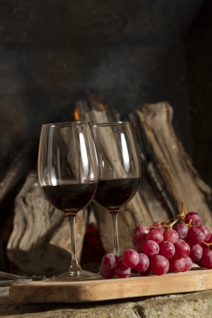 Wine glasses, Grapes, cork and a bottle of wine over a wooden table with fire on the background の写真素材