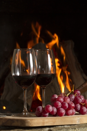 Wine glasses, Grapes, cork and a bottle of wine over a wooden table with fire on the background の写真素材