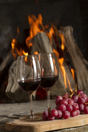 Wine glasses, Grapes, cork and a bottle of wine over a wooden table with fire on the background の写真素材
