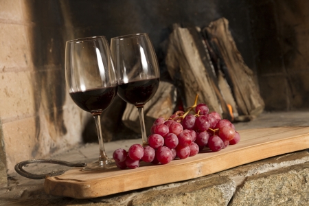 Wine glasses, Grapes, cork and a bottle of wine over a wooden table with fire on the background の写真素材