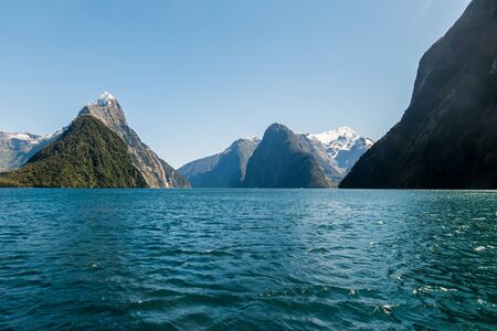 Views on the waters of Milford Sound with the rare sight of the fjord in sunshine. Snow capped mountains in the background fall off steeply into the sea.の写真素材