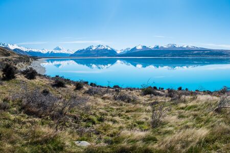 On a windless day the snow capped southern alps mirror in the turquoise water of Lake Pukaki on New Zealand's South Island. The blue, cloudless sky creates a calm and peaceful mood.の写真素材